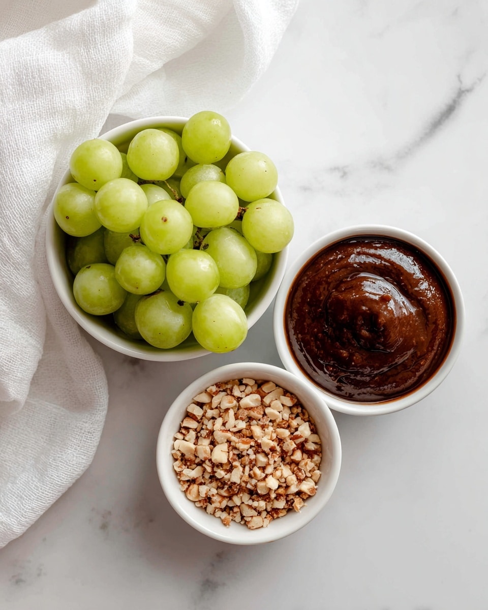 The image shows three small white bowls placed on a white marbled surface with a soft white cloth in the background. The front bowl is filled with small light brown nuts or crushed pieces. The bowl behind it to the left is filled with round, green grapes, tightly packed and shiny. The third bowl, to the right behind the nuts, contains a dark brown thick sauce with a smooth texture. The bowls are arranged close together, creating a simple and clean visual layout. Photo taken with an iphone --ar 4:5 --v 7