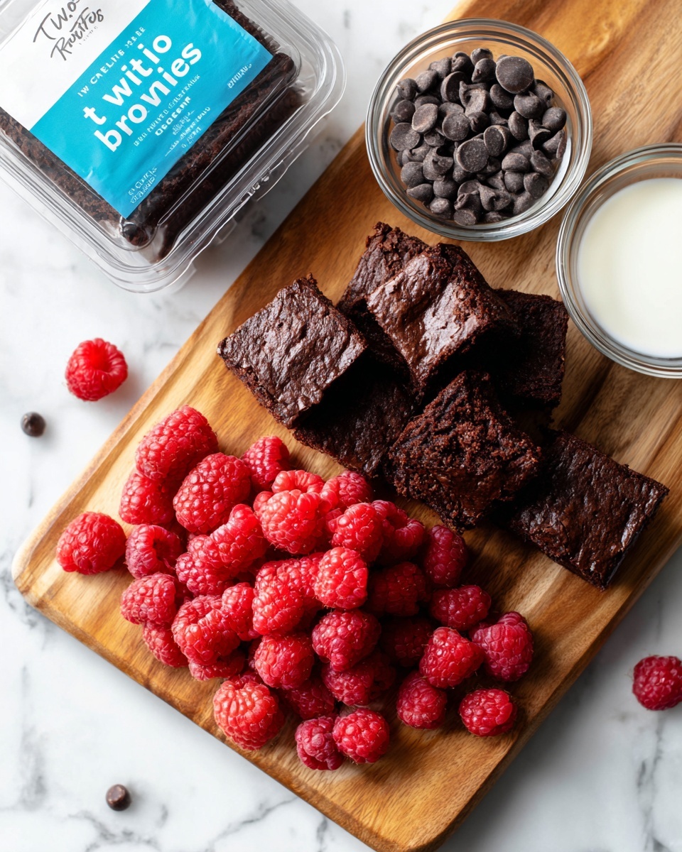 The image shows a wooden board placed on a white marbled surface, with several small dark chocolate brownies arranged on it. In the center, there is a pile of fresh red raspberries with their textured surface visible. Near the top right, there is a small clear glass bowl filled with shiny dark chocolate chips, and next to it, another clear glass bowl contains white cream or milk. To the left side of the board, there is a clear plastic container with a blue label that reads