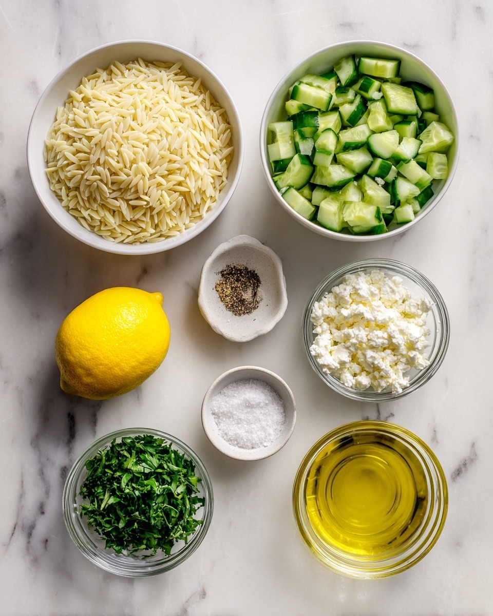 The image shows seven items arranged on a white marbled surface: a white bowl at the top filled with pale yellow orzo pasta, a white bowl on the right containing bright green chopped cucumbers, a whole yellow lemon placed to the left of the cucumber bowl, a small white dish with ground black pepper and salt above the lemon, a small clear glass bowl with crumbled white feta cheese below the lemon, another clear glass bowl with chopped fresh green herbs below the feta cheese, and a clear glass bowl filled with golden-yellow olive oil to the right of the herbs. photo taken with an iphone --ar 4:5 --v 7