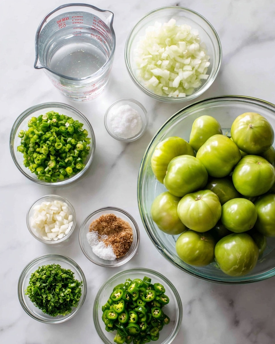 The image shows a top view of several clear glass bowls arranged neatly on a white marbled surface, each containing different ingredients. On the right, a large clear glass bowl is filled with whole green tomatoes, smooth and shiny with a pale green color. To the left and slightly above, there is a clear glass measuring cup with clear water filled just below the top. Below the measuring cup, smaller bowls hold finely chopped green herbs, bright green finely chopped jalapeño peppers, a mix of white salt and light brown spice, finely chopped white onions, minced garlic, and more chopped green herbs. The colors vary from white to different shades of green and light brown, all presented clearly and cleanly with no utensils visible. The scene is well lit with soft natural light highlighting the freshness of the ingredients photo taken with an iphone --ar 4:5 --v 7