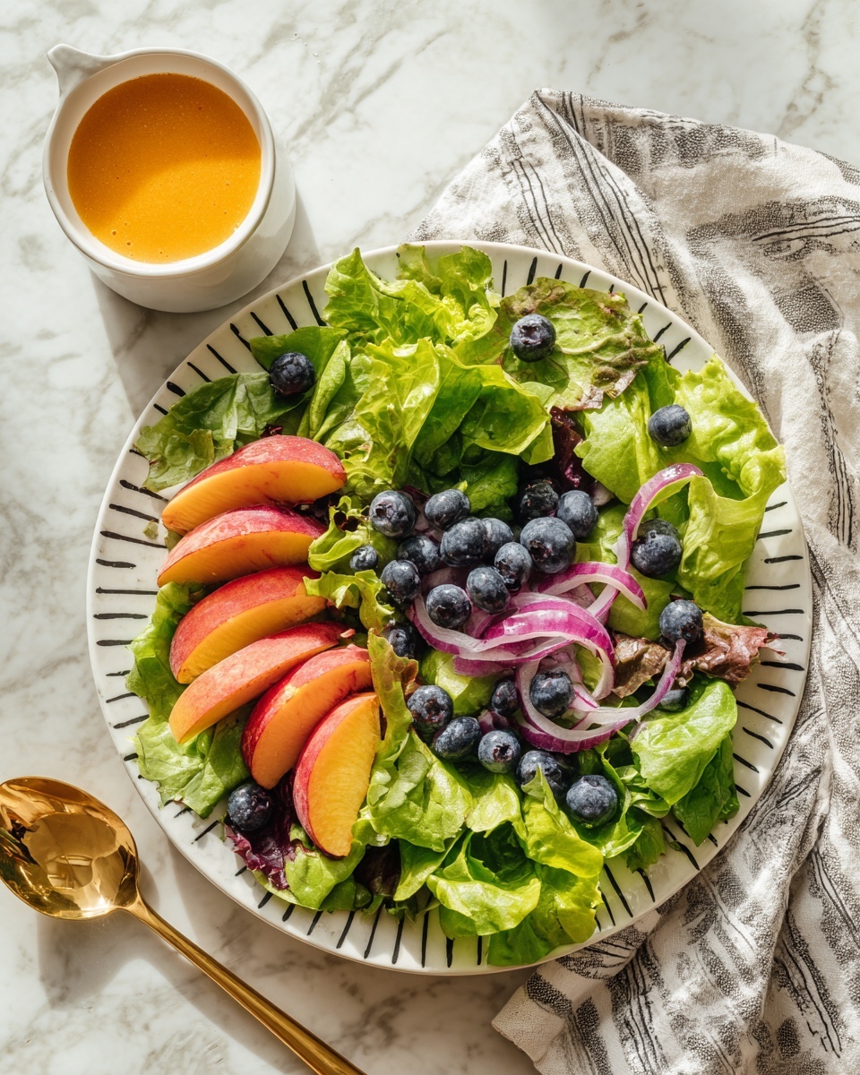 A white plate with black design holds a fresh salad made of three main layers: the bottom layer is large, bright green lettuce leaves, the middle layer has wedges of reddish-pink peaches with smooth texture, and the top layer features a mix of small, plump blueberries and thin purple-red onion slices. The salad has a slight sheen of dressing, and a small white cup filled with orange dressing sits to the left on a white marbled surface. To the right, a gold spoon rests on a gray and white cloth. The scene is bright with natural light, showing clear and vivid colors. photo taken with an iphone --ar 4:5 --v 7