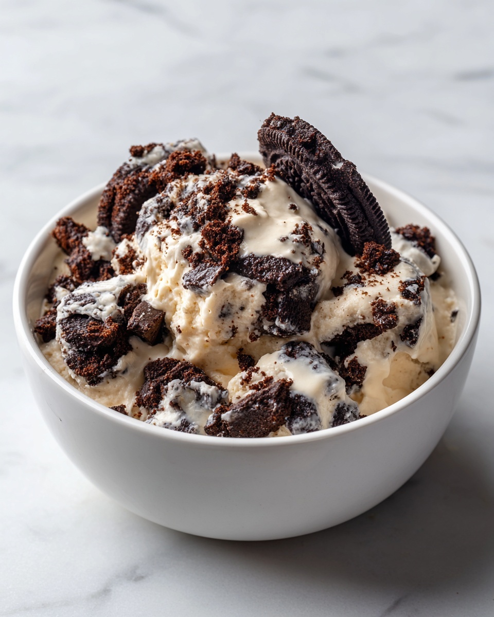 The image shows a white bowl filled with a dessert made of broken dark chocolate cookies layered on top of a creamy light brown mixture. The top layer is uneven with many small cookie pieces and larger chunks, showing a mix of dark brown and white from the cookie cream filling. One larger cookie piece is propped up slightly on the side, revealing a thick white cream inside. The bowl sits on a white marbled surface. photo taken with an iphone --ar 4:5 --v 7