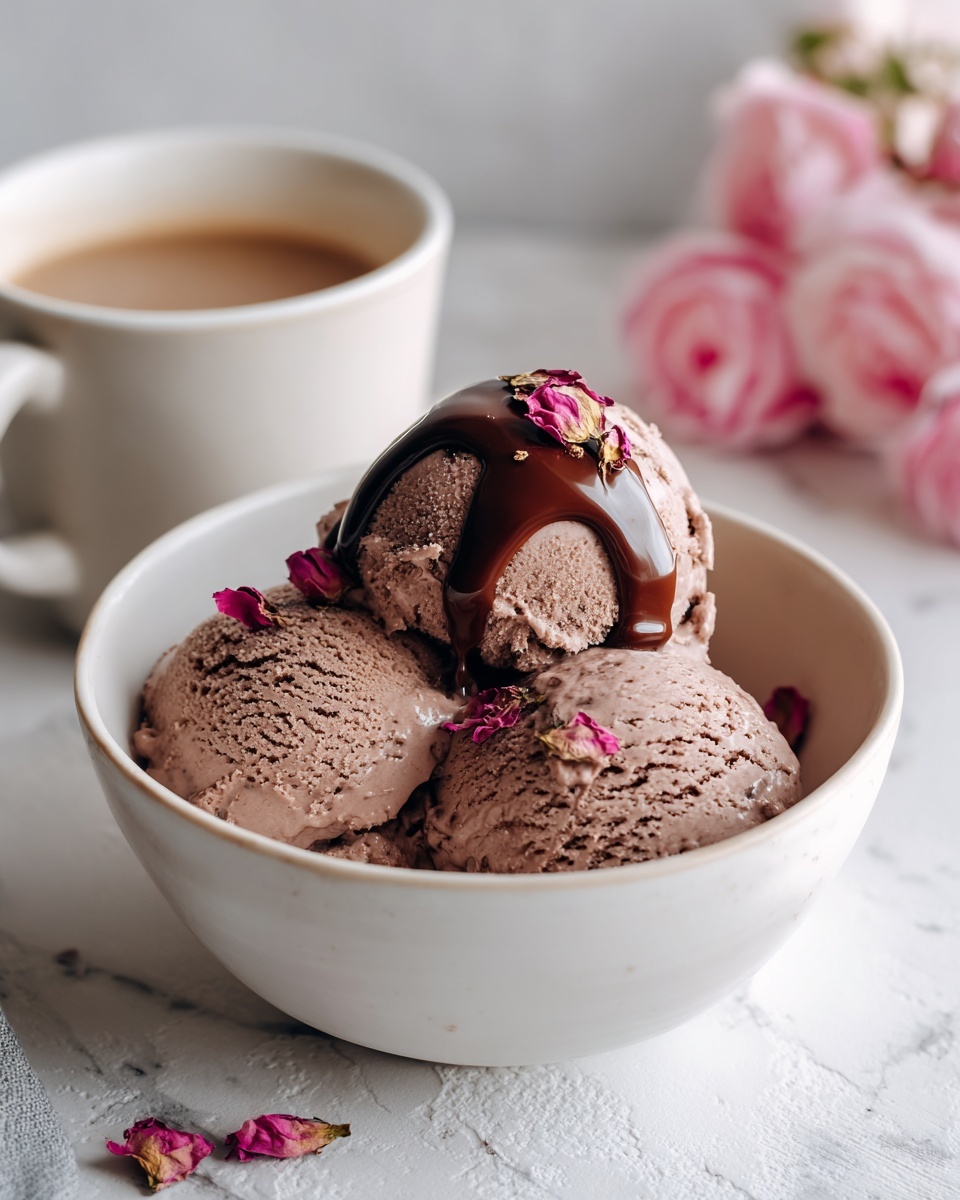 The image shows a white bowl filled with three scoops of chocolate ice cream, each scoop having a rough, creamy texture. A smooth layer of melted chocolate sauce is drizzled over the top scoop, creating a shiny contrast against the matte ice cream. Small dried pink rose petals are softly scattered on the ice cream and around the bowl, adding delicate color and texture. In the background, there is a white cup filled with a light brown liquid and some blurred pink flowers, all set on a white marbled surface. photo taken with an iphone --ar 4:5 --v 7