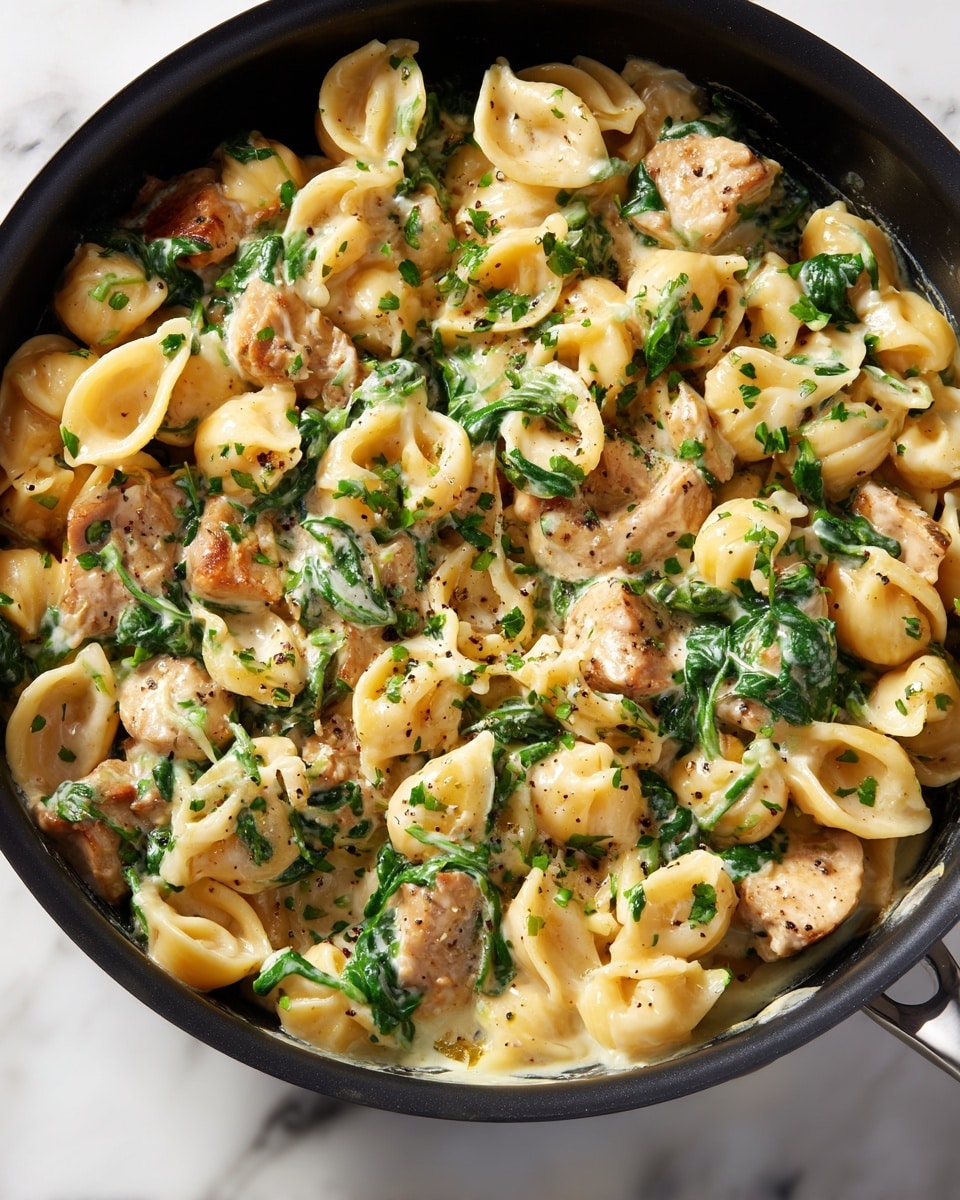 A close-up view of a black pan filled with creamy pasta, featuring short, curved noodles mixed evenly with light beige sliced pieces of meat and bright green leafy spinach. The sauce looks smooth and thick, covering all the ingredients uniformly, with the spinach adding a touch of fresh green color throughout the dish. The pan is set on a white marbled surface. photo taken with an iphone --ar 4:5 --v 7