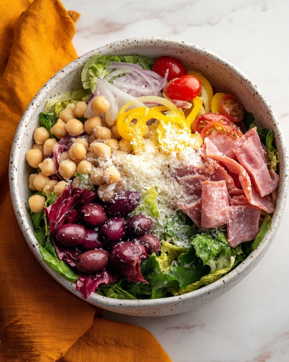 The image shows a large white speckled bowl filled with a colorful salad. The base layer is made up of bright green lettuce and red leafy vegetables. Scattered throughout are round pale yellow chickpeas and dark purple sliced olives. Thin slices of light pink cured meat are mixed in with rings of white onion and sliced yellow pepper. There are also halved small red cherry tomatoes and chunks of white cheese, topped with a sprinkling of grated cheese. The bowl sits on a white marbled surface with an orange cloth napkin nearby. Photo taken with an iphone --ar 4:5 --v 7