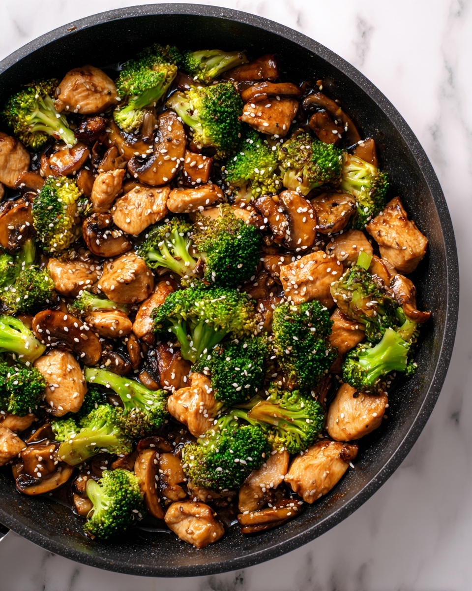 The image shows a close-up of a black skillet filled with cooked pieces of light brown chicken chunks, bright green broccoli florets, and sliced brown mushrooms, all coated in a glossy dark sauce. The chicken pieces are medium-sized and scattered throughout, mixed evenly with the vibrant broccoli and mushrooms. White sesame seeds are sprinkled on top, adding small spots of contrast across the dish. The skillet rests on a white marbled surface, creating a clean and bright background. Photo taken with an iphone --ar 4:5 --v 7