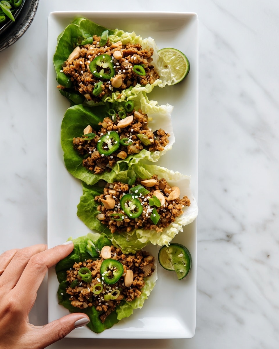 Four green lettuce cups are lined up on a long white rectangular plate on a white marbled surface. Each cup is filled with a mixture of finely chopped browned meat and vegetables, topped with cashew pieces, white sesame seeds, and a round slice of fresh green chili. The filling has a crumbly texture with a mix of light brown and beige colors. A woman's hand is reaching towards one of the cups, creating a casual, inviting scene. Photo taken with an iphone --ar 4:5 --v 7