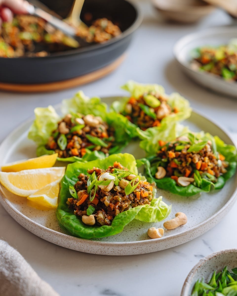 A white round plate holds five fresh green lettuce leaves, each carefully shaped into a cup and filled with a colorful mix of ground meat, small diced orange carrots, and whole light brown cashews. The mixture is topped with thinly sliced green scallions, adding a fresh bright touch. Two lemon wedges sit on the side of the plate, adding a pop of yellow. The plate rests on a white marbled surface, and a dark pan with the same filling can be seen in the background along with a woman's hand holding a utensil nearby. photo taken with an iphone --ar 4:5 --v 7