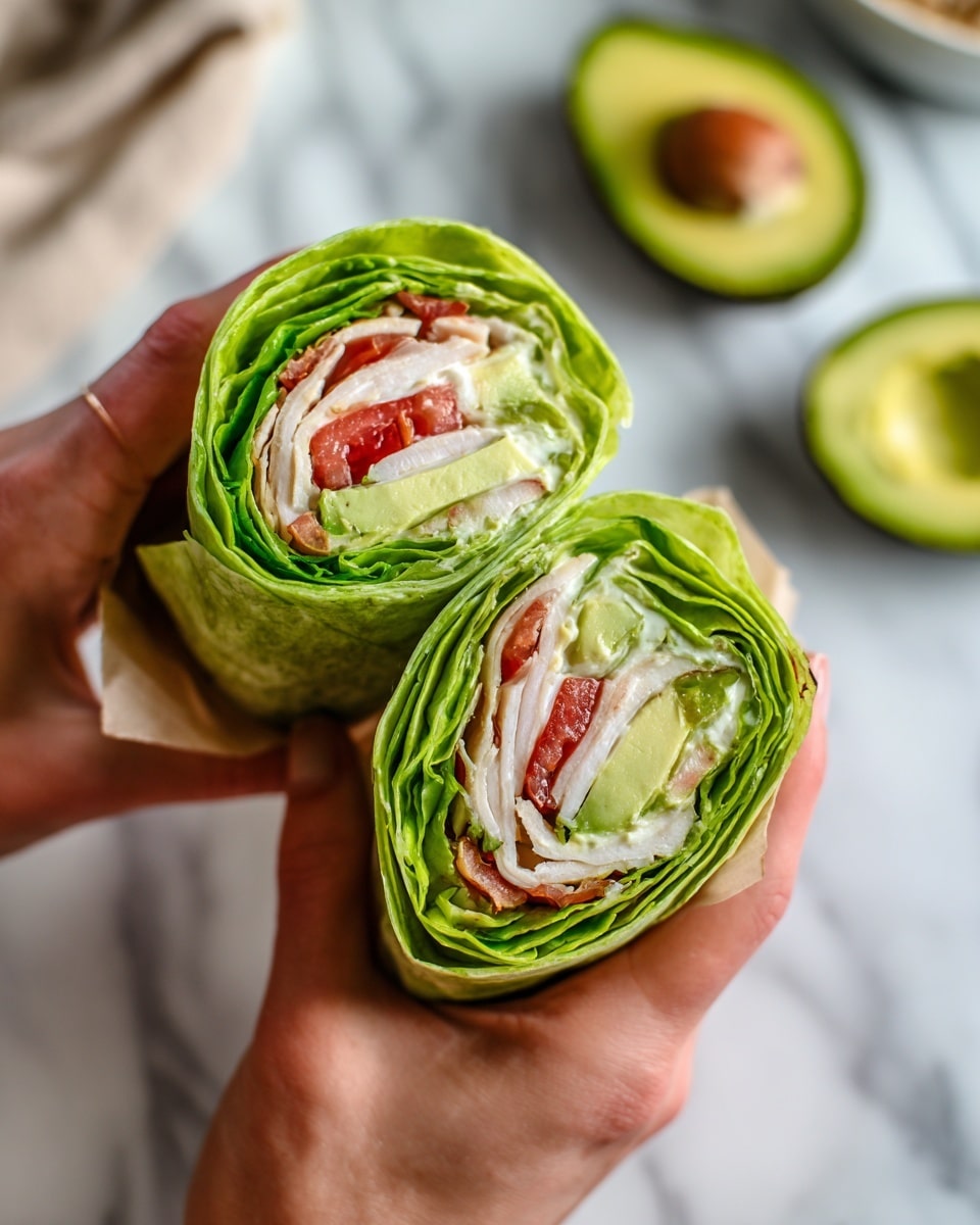A woman's hands are holding a wrap cut in half, showing multiple layers inside. The outer layer is bright green lettuce wrapping the filling tightly. Inside, there are slices of white turkey or chicken, thin layers of red tomato, smooth green avocado, and creamy white sauce spread within. The wrap looks fresh and colorful against a white marbled surface with an avocado half and some dishes blurred in the background. The texture of the lettuce is crisp, and the smooth layers inside add contrast. photo taken with an iphone --ar 4:5 --v 7