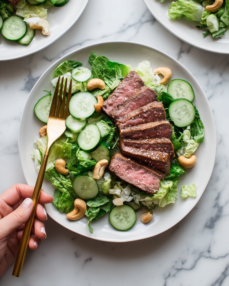A white round plate holds a salad with several layers: a base of chopped green lettuce in varied shades, lightly textured with some crisp edges, topped with thinly sliced cucumber rounds that are light green with darker green rinds scattered across the salad. On top of this sits a neat stack of medium-rare beef slices arranged in a fan shape, showing a warm pinkish center with darker brown edges. Some whole cashew nuts add a crunchy texture and light tan color contrast on the salad. A gold fork rests on the left side of the plate, with a woman's hand holding it. The plate is placed on a white marbled surface with other similar plates and pieces of cucumber around. photo taken with an iphone --ar 4:5 --v 7