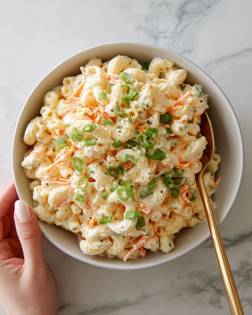 A close-up view of a large bowl filled with creamy macaroni salad showing three main layers: a base layer of small elbow macaroni pasta coated in a smooth and thick white dressing, mixed evenly with thin orange carrot strips that add texture and color contrast throughout, topped with scattered bright green sliced scallions adding freshness and a pop of color on the top layer. The bowl is white and placed on a white marbled surface. A shiny gold spoon rests inside the bowl, partially submerged in the salad, and a woman's hand is visible holding the spoon on the left side of the image. photo taken with an iphone --ar 4:5 --v 7
