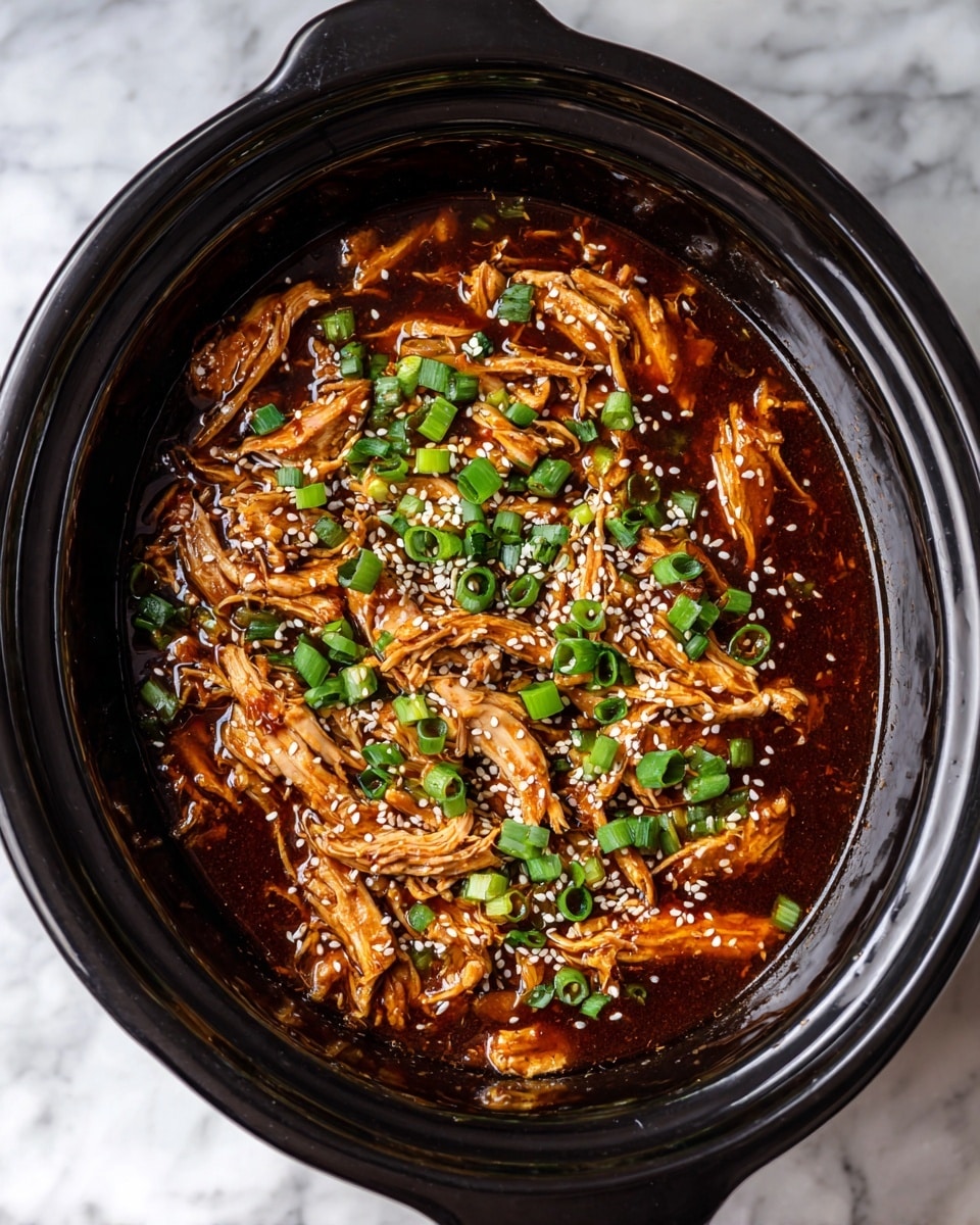 The image shows a slow cooker filled with shredded cooked chicken pieces soaked in a dark brown sauce, creating a glossy and thick texture. The chicken is topped with small, bright green chopped scallions and white sesame seeds scattered evenly over the surface. The cooker is black and contrasts with the rich colors of the food, placed on a white marbled surface. The overall view is close up and focused on the details of the tender chicken and fresh garnishes photo taken with an iphone --ar 4:5 --v 7