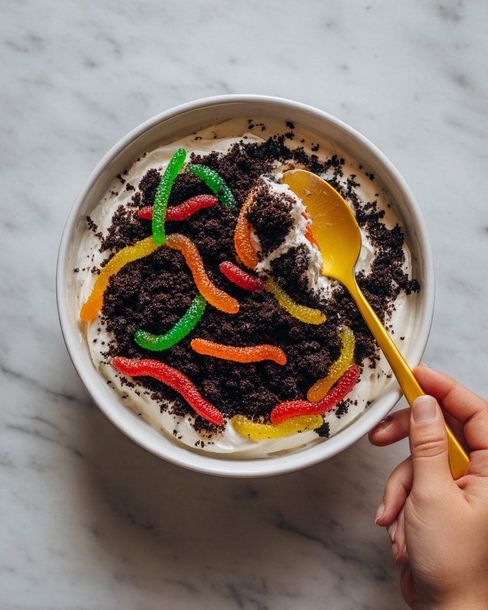 The image shows a red bowl filled with crumbled dark brown cookie pieces, with several colorful gummy worms placed around the bowl and nestled among the cookie crumbs. A yellow spoon is lifting a scoop of white cream covered with more crumbled cookie pieces, with a red gummy worm partly visible on the spoon. The cream looks soft and fluffy, contrasting with the rough texture of the cookie crumbs and the smooth, translucent gummy worms. The scene gives the impression of a playful dirt pudding dessert. Photo taken with an iphone --ar 4:5 --v 7