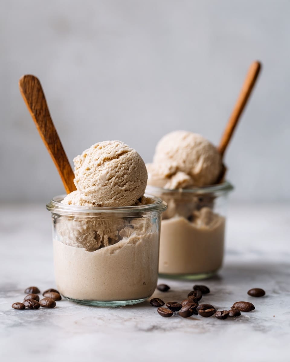 Two clear glass jars filled with several scoops of light brown ice cream that looks creamy and smooth. The jar in the foreground has a wooden spoon inside, while the jar behind shows more of the ice cream's texture. Scattered around the jars are a few dark brown coffee beans. The scene is set on a white marbled surface with a soft, light background. photo taken with an iphone --ar 4:5 --v 7