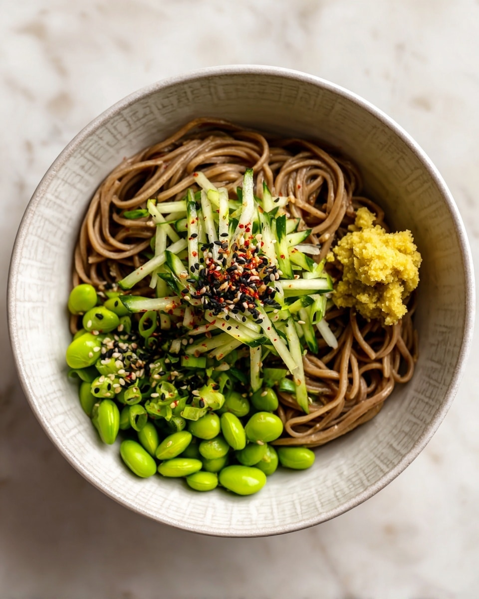 A bowl with a base layer of light brown soba noodles, topped with scattered bright green edamame beans and thin green scallion slices. On top, there is a small pile of thin, pale green cucumber strips sprinkled with red pepper flakes and black and white sesame seeds. At the side of the bowl, there is a small dollop of light yellow ginger paste. The bowl is white with a subtle patterned edge, and it is placed on a white marbled surface. photo taken with an iphone --ar 4:5 --v 7