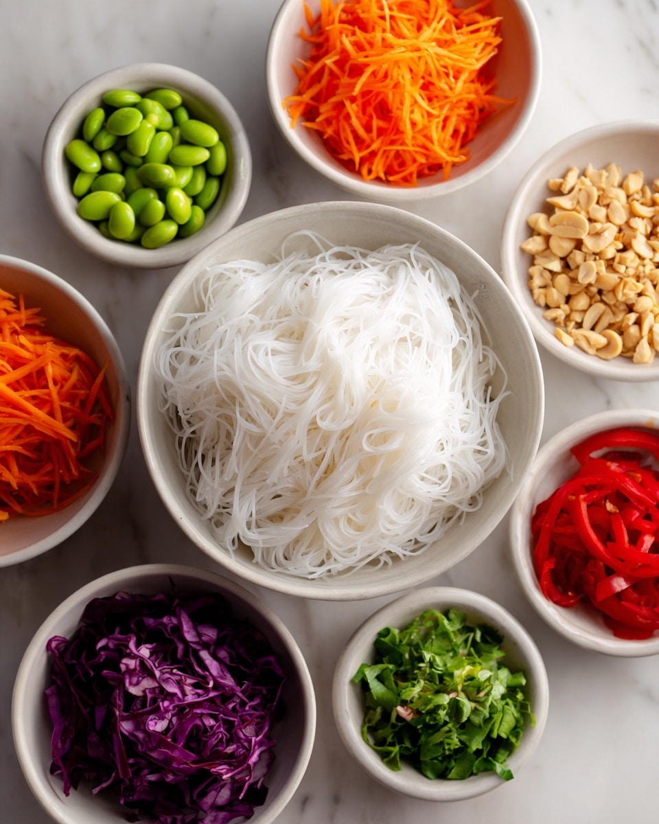 A neat arrangement of small white bowls placed around a larger white bowl filled with white rice noodles in the center on a white marbled surface. The surrounding bowls each hold a different ingredient: bright orange shredded carrots, finely sliced red cabbage with a deep purple color, bright green edamame, thin red pepper strips mixed with carrot strips, finely chopped green herbs, and crushed peanuts. The colors are vivid and fresh, giving a lively and healthy feeling to the image. The lighting is soft and natural, highlighting the textures of each ingredient. photo taken with an iphone --ar 4:5 --v 7