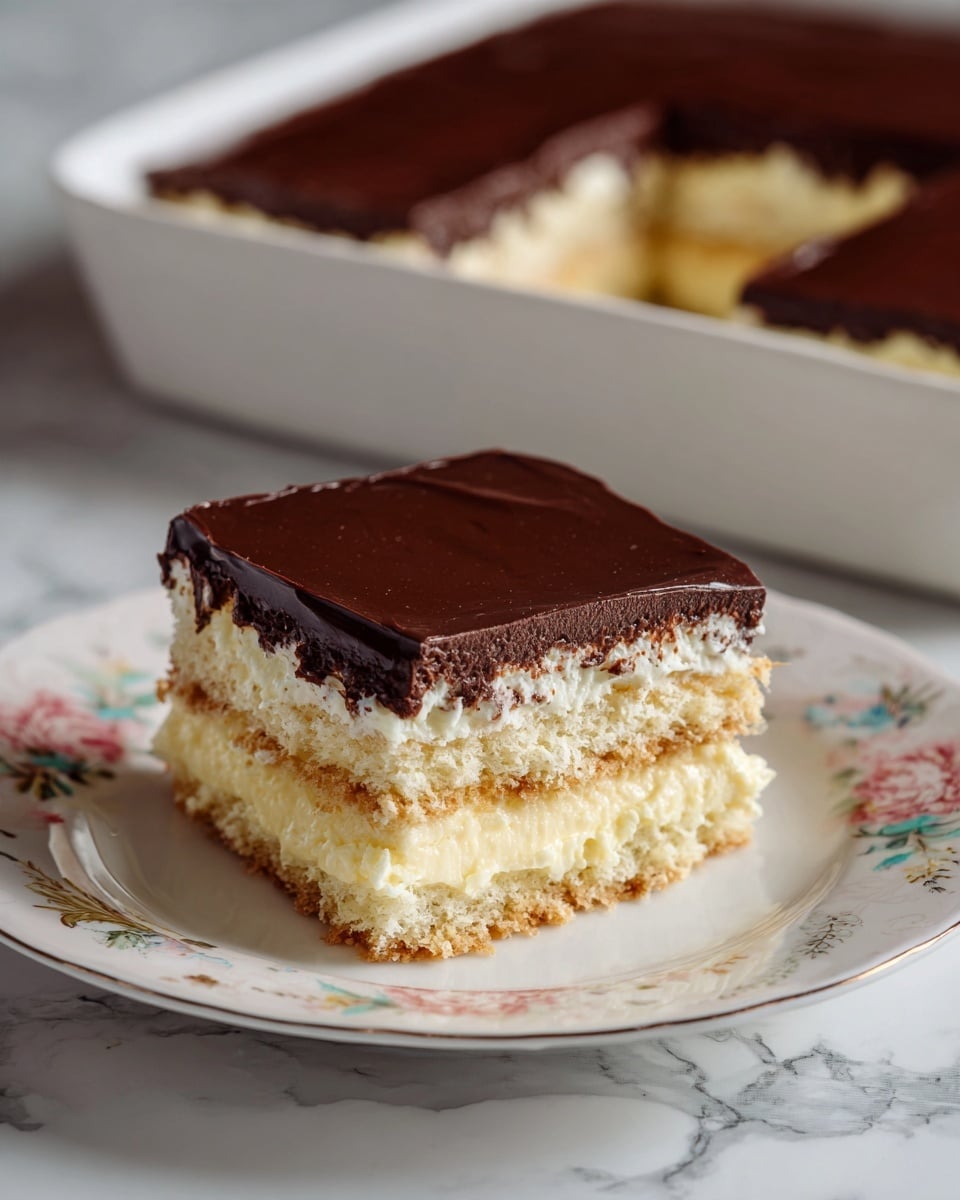 The image shows a piece of layered dessert on a white plate with a soft floral design. The dessert has three layers of light-colored soft cake or cookies separated by creamy beige filling, topped with a smooth, thick dark chocolate layer. Behind the plate, a larger rectangular dish with the same dessert is visible on a white marbled surface. The colors of the dessert layers contrast well, with the dark chocolate topping standing out on top. The texture looks creamy and smooth on the filling, with a slightly crumbly but soft cake layer. Photo taken with an iphone --ar 4:5 --v 7