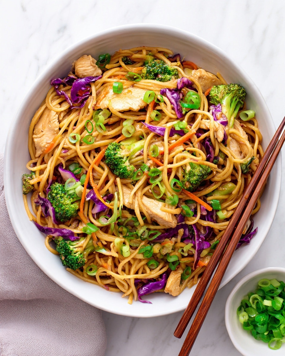A white bowl full of stir-fried noodles mixed with chunky pieces of light brown cooked chicken, bright green broccoli florets, thin orange carrot strips, purple cabbage, and light pieces of chopped scallions on top. The noodles are light brown and look soft, tangled with vegetables and chicken in layers. A pair of wooden chopsticks is resting inside the bowl on the right side. Next to the bowl on a white marbled surface is a small white bowl filled with chopped green scallions. The scene is bright and fresh, showing a close-up top view of the dish photo taken with an iphone --ar 4:5 --v 7