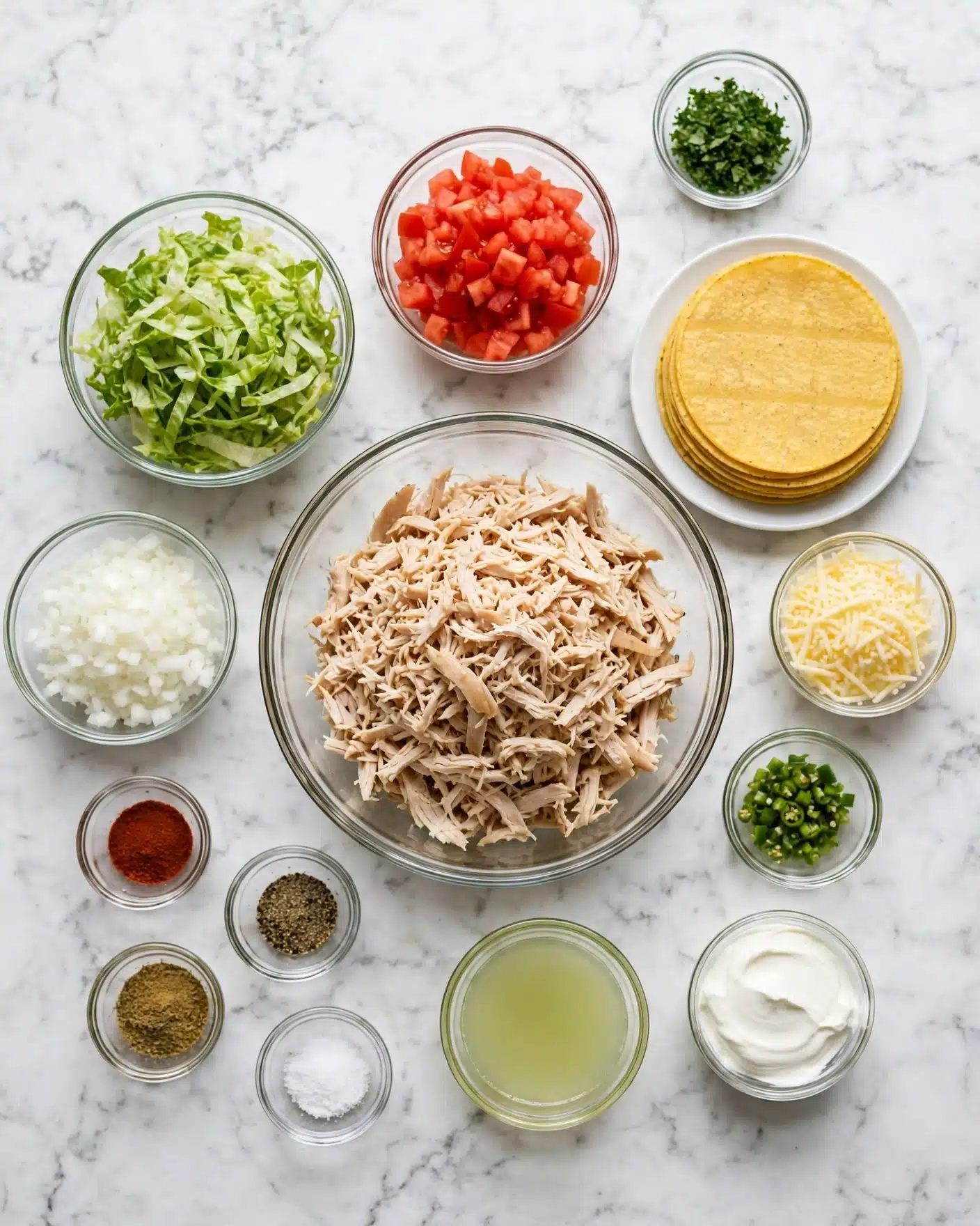 square image The image shows an overhead view of small glass bowls arranged neatly on a white marbled surface, each holding a different taco ingredient. In the center, there is a large clear bowl with shredded cooked chicken. To the left, a bowl with shredded lettuce sits next to a bowl of finely chopped white onion. Above the chicken, a bowl contains bright red diced tomatoes. To the right, a white plate holds a stack of yellow corn tortillas. Smaller bowls around the main ones contain finely chopped green herbs, shredded cheese, diced green chilies, a small bowl of sour cream, a pale green liquid (likely lime juice), and tiny bowls of salt, black pepper, chili powder, and ground cumin. The arrangement is clean and precise, highlighting the fresh ingredients. photo taken with an iphone --ar 4:5 --v 7