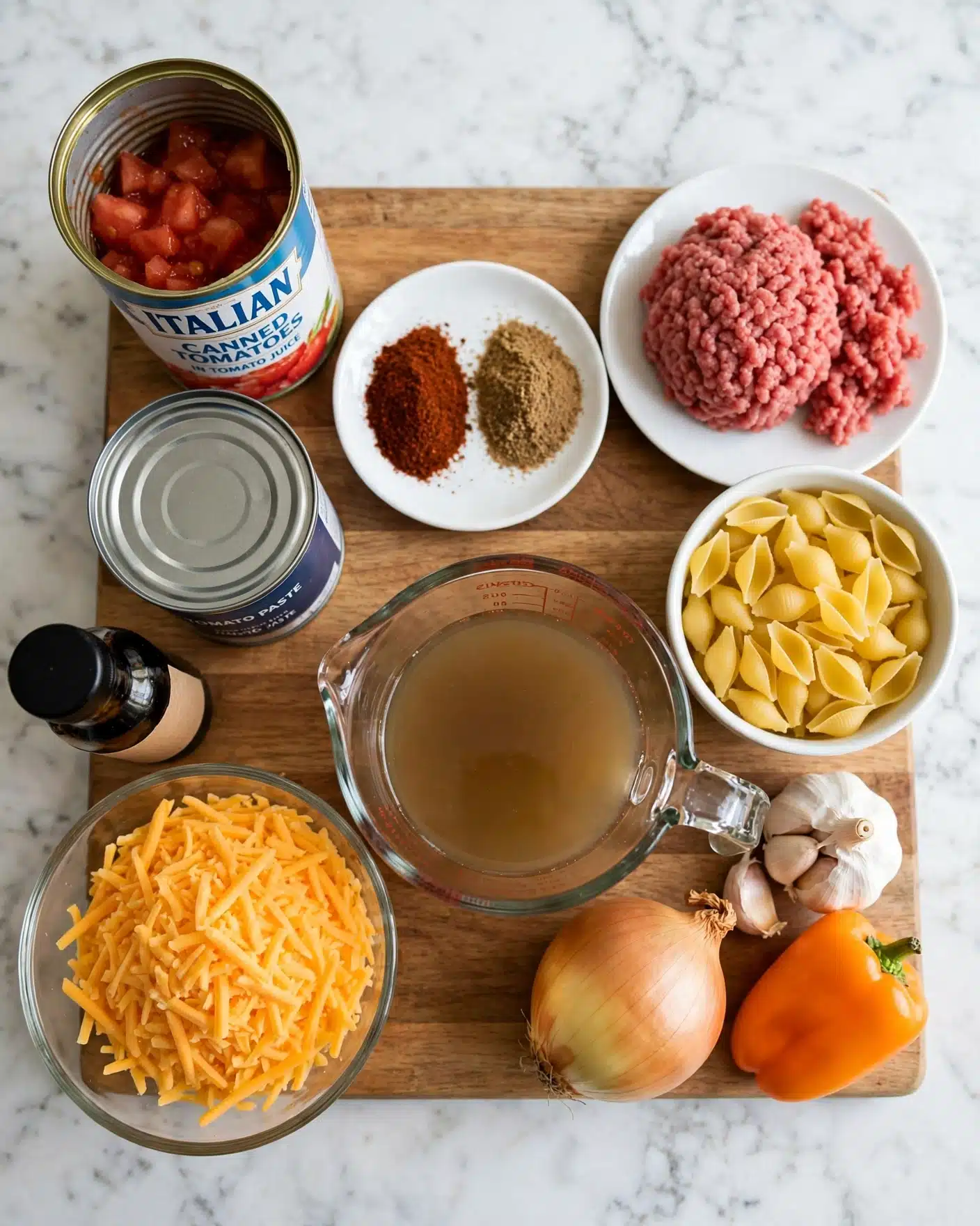 Silly Chili Macaroni Recipe 4 square image The image shows a wooden board placed on a white marbled surface with several cooking ingredients arranged neatly on it. On the top left is an open can of Italian canned tomatoes with a blue and white label. Below it is another closed metal can. Next to the cans is a white small dish holding two types of ground spices: dark red and light brown. To the right of the spices, there is a mound of raw ground meat placed on a white plate. Below the meat is a white bowl filled with yellow uncooked shell pasta. In the bottom left corner, there is a transparent glass bowl filled with finely shredded orange cheddar cheese. Next to the cheese, near the bottom edge, lie a whole yellow onion, a bulb of garlic, and a small orange bell pepper. A clear glass measuring cup with a light brown liquid is placed in the center bottom area. A small bottle with a black cap is at the left edge of the board. The setup is clean and organized, focused on showing raw ingredients for cooking. photo taken with an iphone --ar 4:5 --v 7
